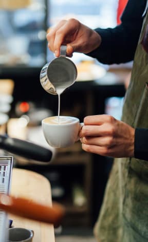 Barista at Coffee Shop Pouring Milk in Coffee Mug